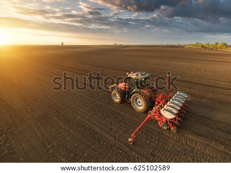 Farmer with tractor seeding - sowing crops at agricultural fields in spring