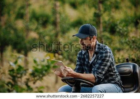 Farmer using digital tablet to inspect fruit trees in orchard.