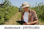A farmer is using a tablet device in his orchard to effectively manage crop production and care