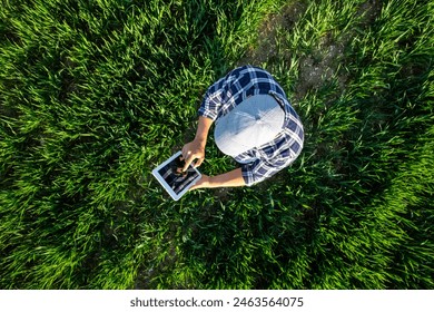 Farmer using tablet in wheat field. View from above of a farmer in blue shirt using a tablet in a young wheat field.High quality photo - Powered by Shutterstock