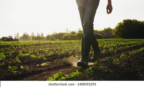A farmer walks across a field in rubber boots on a blurred background of the tractor in motion. Concept of: Rubber boots, Lifestyle, Farmer, Slow Motion, Fields.