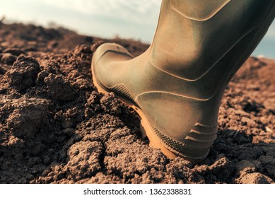 Farmer in wellington rubber boots making first step in field, close up. Beginning of agricultural season and starting of activities on farmland.