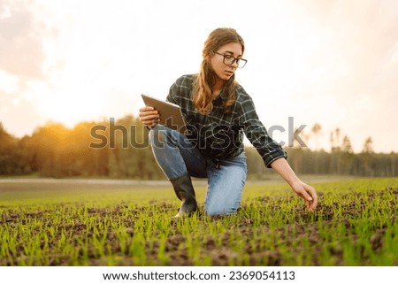 Farmer woman in boots checks the quality of the soil before sowing in her hands with a digital tablet. Woman agronomist in a field of young sprouts. Concept of gardening, ecology, tegnology. 