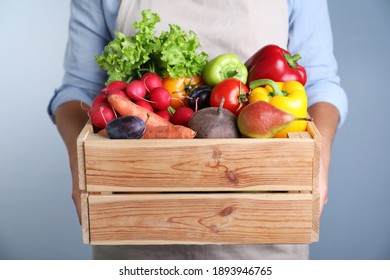 Farmer with wooden crate full of different vegetables and fruits on blue background, closeup. Harvesting time