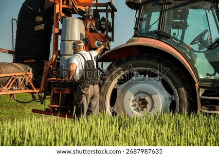 Farmer worker preparing a tractor mounted sprayer in a green agricultural field