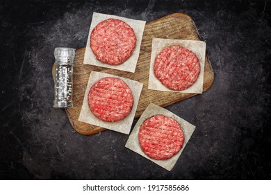 Farmers Beef Pork Burgers And Spice Mill On Wooden Board, Top View. Raw Ground Beef Meat Steak Burger Cutlets On Black Table Background, Overhead View. Homemade Raw Beef Burgers For Barbecue Grill.