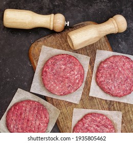 Farmers Beef Pork Burgers And Spice Mill On Wooden Board, Top View. Raw Ground Beef Meat Steak Burger Cutlets On Black Table Background, Overhead View. Homemade Raw Beef Burgers For Barbecue Grill.