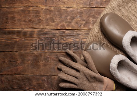 Farming or gardening flat lay background with copy space. Galoshes, garden gloves and sackloth bag on the wooden brown floor background.
