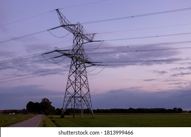 Farmland Field With Silhouette Of Electricity Tower Construction And Power Lines Against A Colourful Magenta Blue Purple Sunset Sky