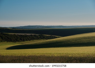 Farmland On A Sunny Evening In The South Downs National Park With The Sun Setting Over The Sussex Weald. Newhaven And Wind Turbines In The Far Distance. Highlights And Shadows On The Fields. No People