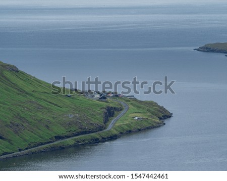 Faroe Islands. View over the village on the slope of hills. Ocean. Cloudy weather. Hazy landscape.