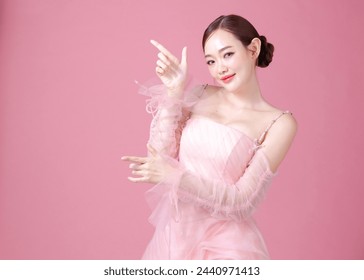 Fascinating fun joyful young woman of Asian wears sweet pink flower dress pose gesture pointing finger aside to copy space isolated on plain pastel light pink background Lady portrait in studio. - Powered by Shutterstock