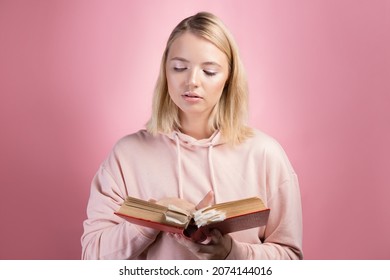 Fascinating reading, serious study of educational materials, an open book with a large number of bookmarks in the hands of a student. A young woman in a pink hoodie with a textbook in her hands,