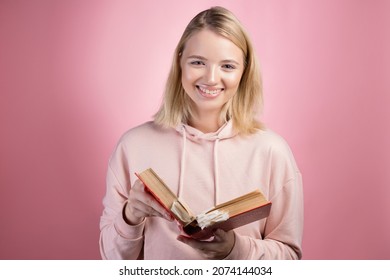 Fascinating reading, serious study of educational materials, an open book with a large number of bookmarks in the hands of a student. A young woman in a pink hoodie with a textbook in her hands,