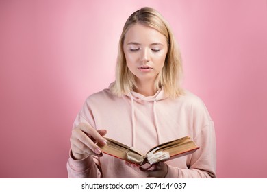Fascinating reading, serious study of educational materials, an open book with a large number of bookmarks in the hands of a student. A young woman in a pink hoodie with a textbook in her hands,