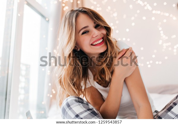 部屋でポーズをとっている 薄化粧の魅力的な白い女の子 家の窓際に座って微笑む若い嬉しい女性 の写真素材 今すぐ編集