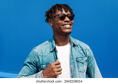 fashion african man in sunglasses in trendy modern clothes posing against the background of a blue building, on the street