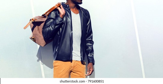 Fashion African Man Wearing Black Biker Leather Jacket Holds Bag Looking Away Over Gray Background