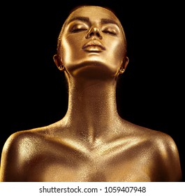 Fashion art Golden skin Woman face portrait closeup. Model girl with holiday golden Glamour shiny professional makeup. Gold jewellery, jewelry, accessories. Beauty gold metallic body, Lips and Skin. 