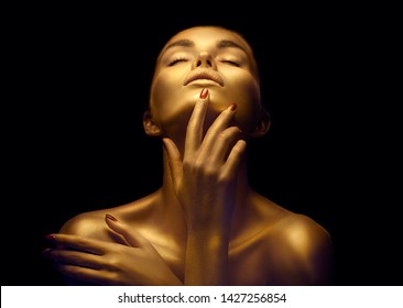 Fashion Art Golden Skin Woman Face Portrait Closeup. Model Girl With Holiday Golden Glamour Shiny Professional Makeup. Gold Jewellery, Jewelry, Accessories. Beauty Gold Metallic Body, Lips And Skin