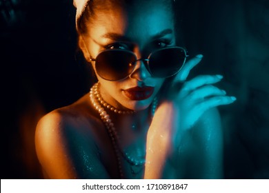 Fashion art portrait of beauty model woman in bright lights and colourful. Gorgeous girl, close up of a female with sunglasses and jewerly. Night life concept. Mechanically blurred