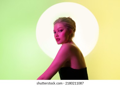 Fashion Art Portrait Of Woman In Neon Color Light  Looking To The Camera On Green Neon Background. Behind The Girl On The Wall Is A Circle From A Spotlight.