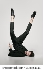 Fashion and Art. A stylish brunet man fashion model in an elegant black suit poses on a white background upside down with his legs up. Full-length studio portrait.