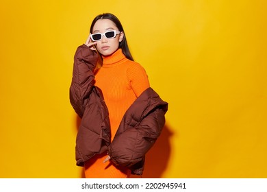 Fashion asian female model. Orange dress, down jacket, white boots, sunglasses. Asian fashion