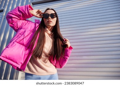 Fashion asian female model outdoor. Pink down jacket, blue skirt, pink sweater, sunglasses. Monochromatic look. Urban city streets.