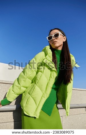 Fashion asian female model outdoor. Green down jacket, green skirt, green sweater, sunglasses. Monochromatic look. Urban city streets.