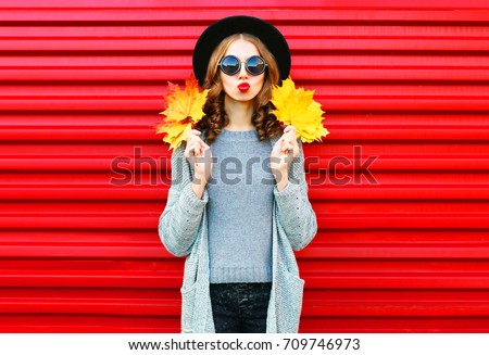 Fashion autumn portrait woman with yellow maple leaves on a red background