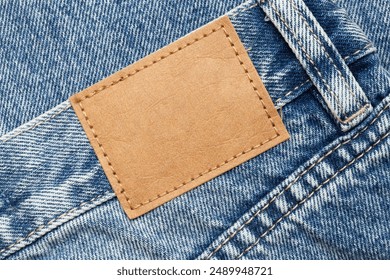 Fashion background with empty copy space for graphic design. Blank leather label tag. Blue jeans denim texture with thread sew lines. Brown clothing tag. - Powered by Shutterstock