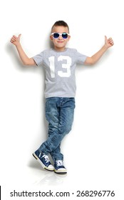 Fashion beautiful little boy in sunglasses t-shirt jeans standing and giving thumbs up sign over white background