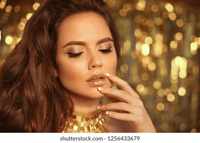 Fashion Beauty Girl Portrait Isolated On Golden Christmas Lights Glitter Bokeh Background. Glamour Makeup. Gold Jewelry. Hairstyle. Alluring Brunette With Glittering Lipstick And Manicured Nails.