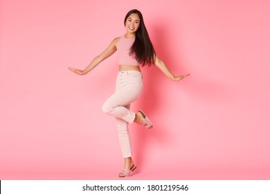 Fashion, Beauty And Lifestyle Concept. Silly And Glamour Beautiful Asian Girl Posing Coquettish Over Pink Background, Smiling And Raising Foot, Advertisement Of Women Selfcare And Shopping