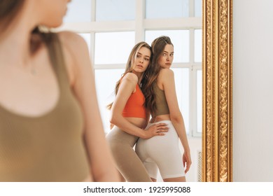 Fashion beauty models two sisters twins beautiful girls with long hair in sport wear looking to mirror in bright studio - Shutterstock ID 1925995088