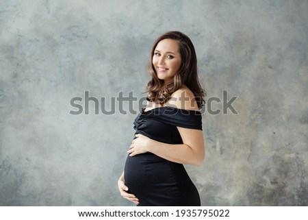 Fashion beauty portrait of happy pregnant woman in black dress on gray background