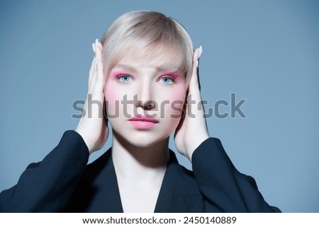 Fashion and beauty shot. A beautiful girl fashion model with a blonde short haircut and bright pink makeup poses in a black suit. Gray studio background. Makeup and hairstyle. 