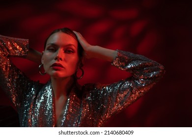 Fashion, beauty studio portrait of confident woman with wearing trendy sequin dress, silver hoop earrings, posing in red light. Copy, empty space for text