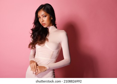 Fashion Beauty Woman Has Long Curl Black Hair Looks At Camera And Express Feeling Smile Happy. Portrait Of Asian Girl Show Tanned Skin Wear Pink Skinny Dress Over Pink Color Block Background