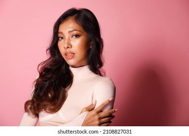 Fashion Beauty Woman Has Long Curl Black Hair Looks At Camera And Express Feeling Smile Happy. Portrait Of Asian Girl Show Tanned Skin Wear Pink Skinny Dress Over Pink Color Block Background