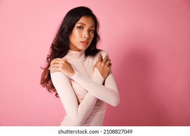 Fashion Beauty Woman Has Long Curl Black Hair Looks At Camera And Express Feeling Smile Happy. Portrait Of Asian Girl Show Tanned Skin Wear Pink Skinny Dress Over Pink Color Block Background