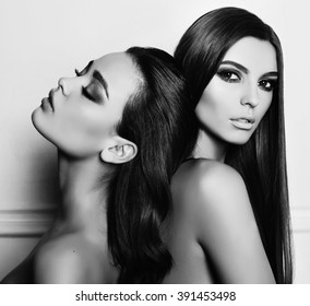 fashion black and white photo of two beautiful girls with dark hair and evening makeup, posing in studio