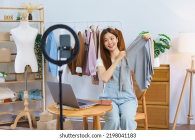 Fashion blogger concept, Young Asian women hold clothes to present and selling on video streaming. - Shutterstock ID 2198041183