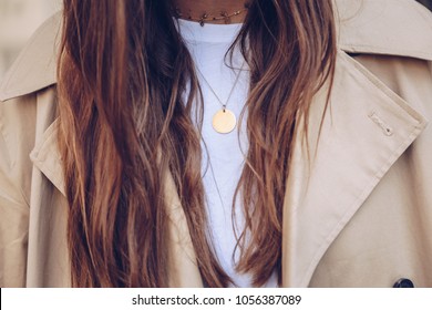 fashion blogger outfit details. fashionable woman wearing a beige trench coat, white t shirt, choker necklace and a round gold chain necklace. detail of a perfect fall fashion outfit.
