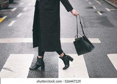 fashion blogger outfit details. fashionable woman wearing a black oversized coat, black jeans, black ankle shoes a black trendy handbag. detail of a perfect fall fashion outfit. 
