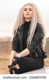 Fashion Blonde Long Curly Hair Lady Sitting On White Automobile Hood Surrounded By Dry Yellow Grass Natural Field. Glamour Rock Woman Posing On Car Transportation Enjoy Freedom Travel Journey Scenery