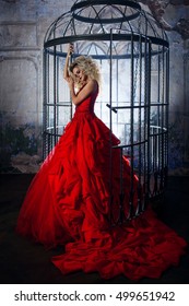 Fashion blonde in red dress with fluffy skirt near the birdcage, concept of liberation