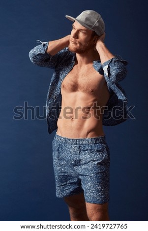 Fashion, body or model with six pack in studio on a blue background in an open unbuttoned shirt. Thinking, chest or handsome male person posing on color wall for masculine style with a trendy cap Foto d'archivio © 