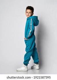 Fashion Boy Child In Warm Sportswear Suit Standing Half Turn Looking At Camera. Male Kid Advertising Sportive Outerwear Clothing. Sportive Fashionable Outfit. Studio Shot Portrait On Grey Background